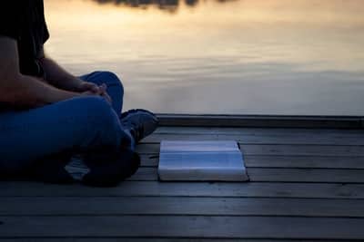 man reading Bible on a dock over looking a lake