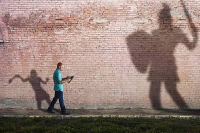 man reading bible with shadows of David and Goliath behind him