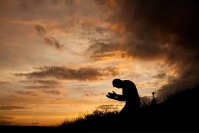 man kneeling and praying during sunset