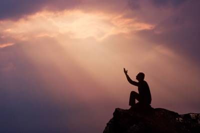man on mountain praying with hands lifted