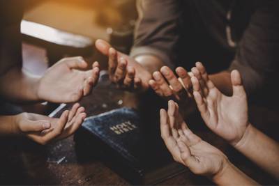 People around a Bible with hands facing upward
