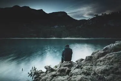 man sitting on rock in front of lake