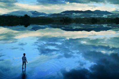 little boy appearing to walk on water with clouds reflecting on the clear water