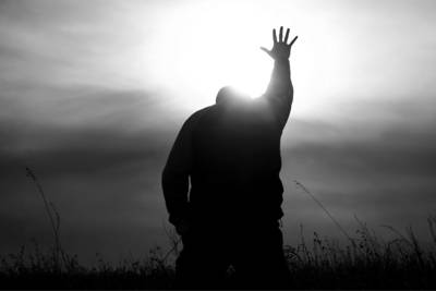 man praying on knees with one hand lifted in the air. Picture is black and white.
