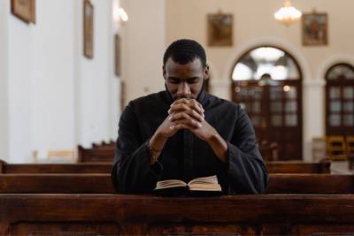 man sitting in pew, praying with Bible open