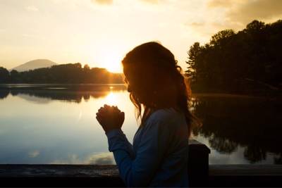 women praying near lake with sunset in background