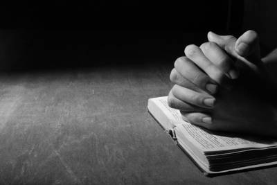 hands folded on bible. black and white picture.