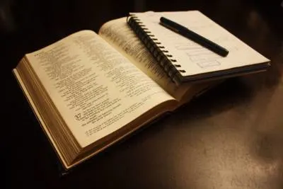 bible open with notepad and pen resting on top.