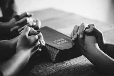 Bible on table. Folded hands all around the Bible.