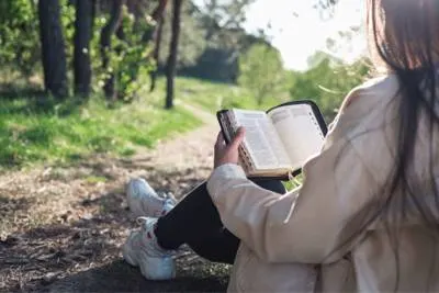person sitting on hiking trail reading bible.