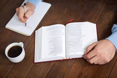 person writing in journal with bible on table and coffee