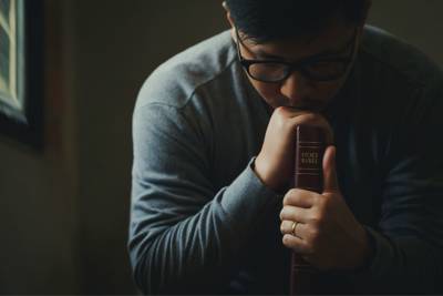 man holding Bible while praying.
