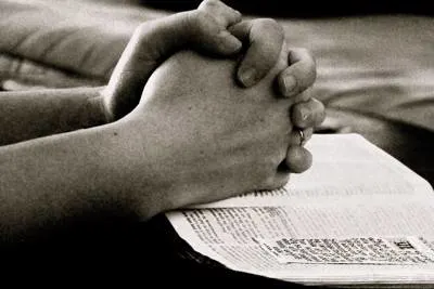 hands folded, resting on Bible.